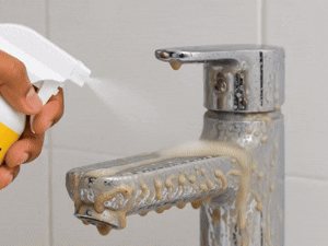 Tap with white hard-water stains being sprayed with Scrubsy Bathroom Cleaner